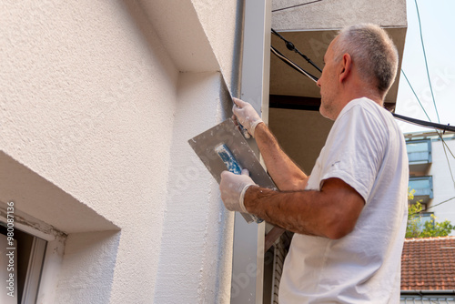 Construction worker applying final decorative facade plaster paste. Home renovation. Builders apartment improvement or restoration works. photo