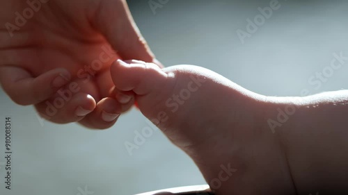 A close-up of a newborn’s tiny feet gently cradled by the mother’s hand. The mother softly strokes the baby’s toes, capturing a tender and intimate moment of care and love.