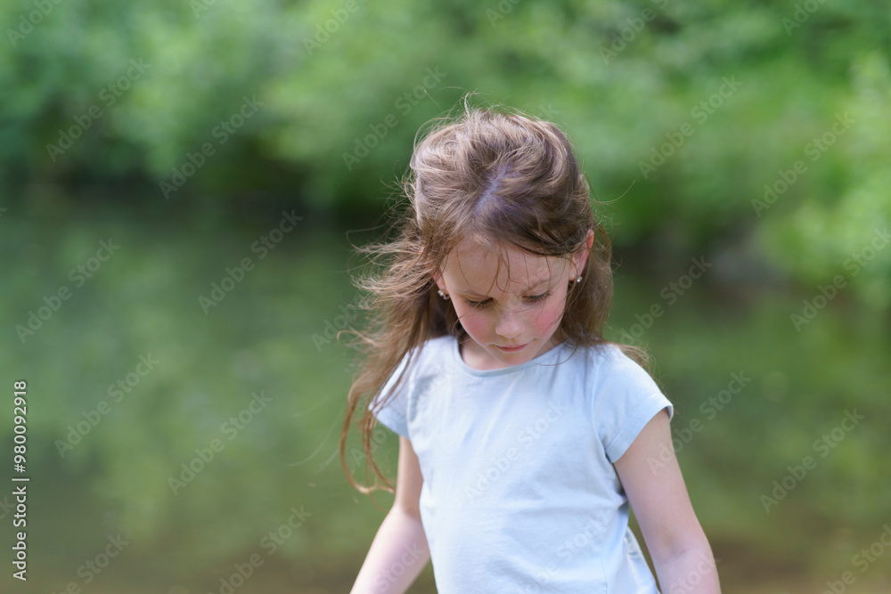 Little cute preschool girl in a T-shirt plays on the background of a pond. Happy childhood concept outdoors Little cute preschool girl in a T-shirt plays on the background of a pond. Happy childhood concept outdoors