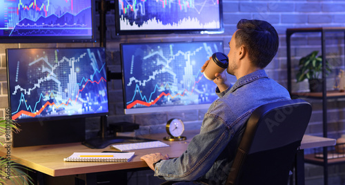 Male trader drinking coffee in office at night, back view