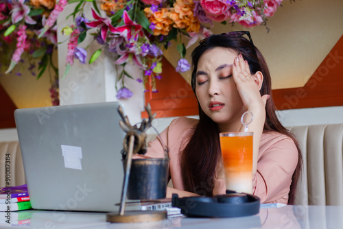 expression of beautiful young indonesia female close eyes hand hold head hurt, headache dizzy sitting on sofa in indoor coffee shop. for health content, lifestyle, education, advertising photo