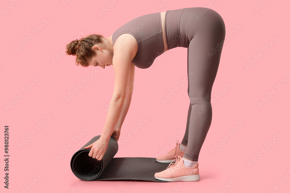 Fototapeta premium Sporty young woman with yoga mat on pink background