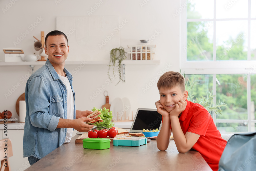Happy father packing school lunchbox for his little son in kitchen Happy father packing school lunchbox for his little son in kitchen