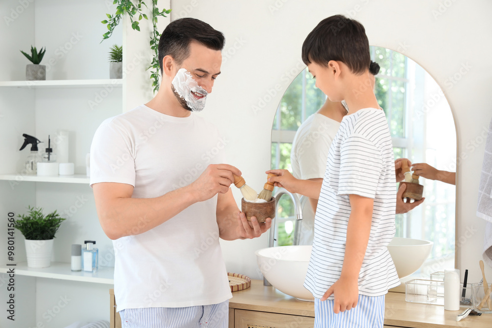 Happy father and his little son with brushes applying shaving foam on their faces in bathroom Happy father and his little son with brushes applying shaving foam on their faces in bathroom