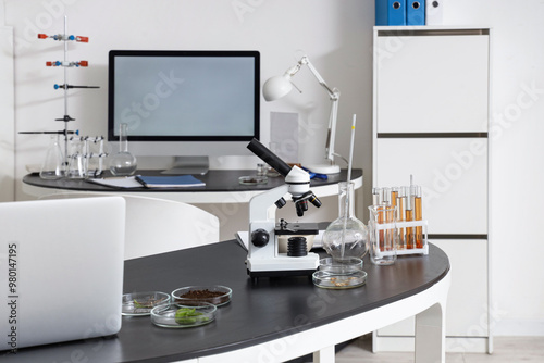 Microscope with chemical glassware and laptop on table in laboratory