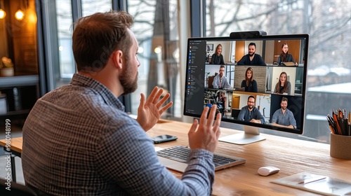 A man participates in a virtual meeting through video conferencing on a large screen, engaging with remote colleagues. photo