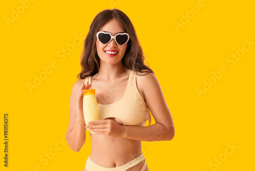 Young Asian woman in sunglasses with sunscreen cream on yellow background