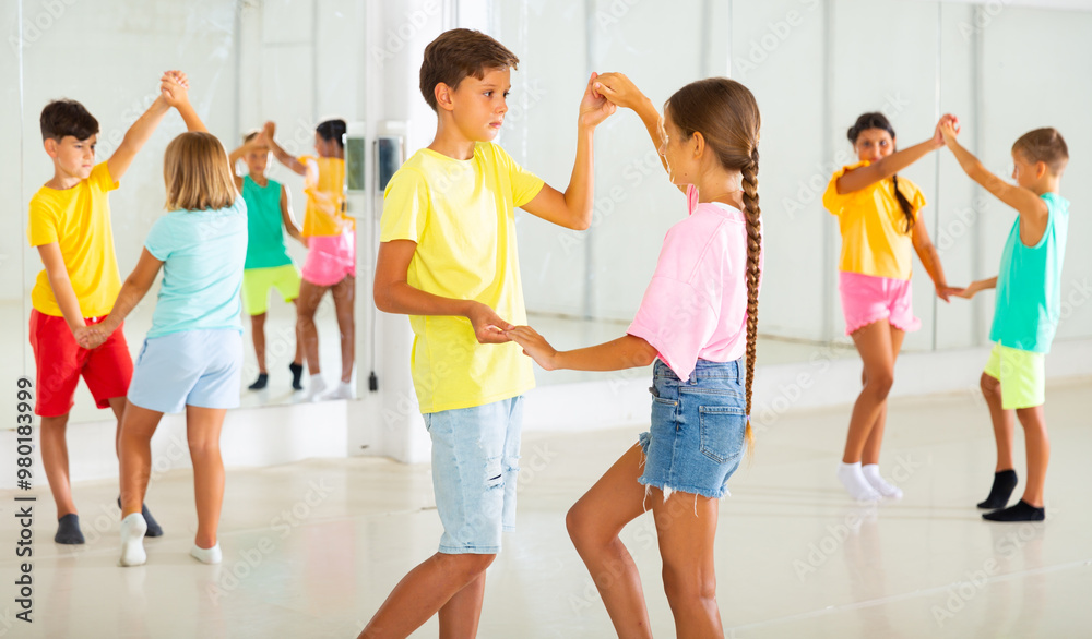 Fototapeta premium Kids in pairs exercising salsa moves together during group dance class.