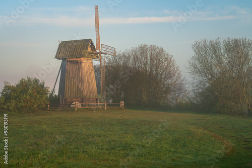 View of an ancient wooden windmill on the banks of the Sorot River on a foggy summer morning, Mikhailovskoye, Pushkinskiye Gory, Pskov region, Russia photo