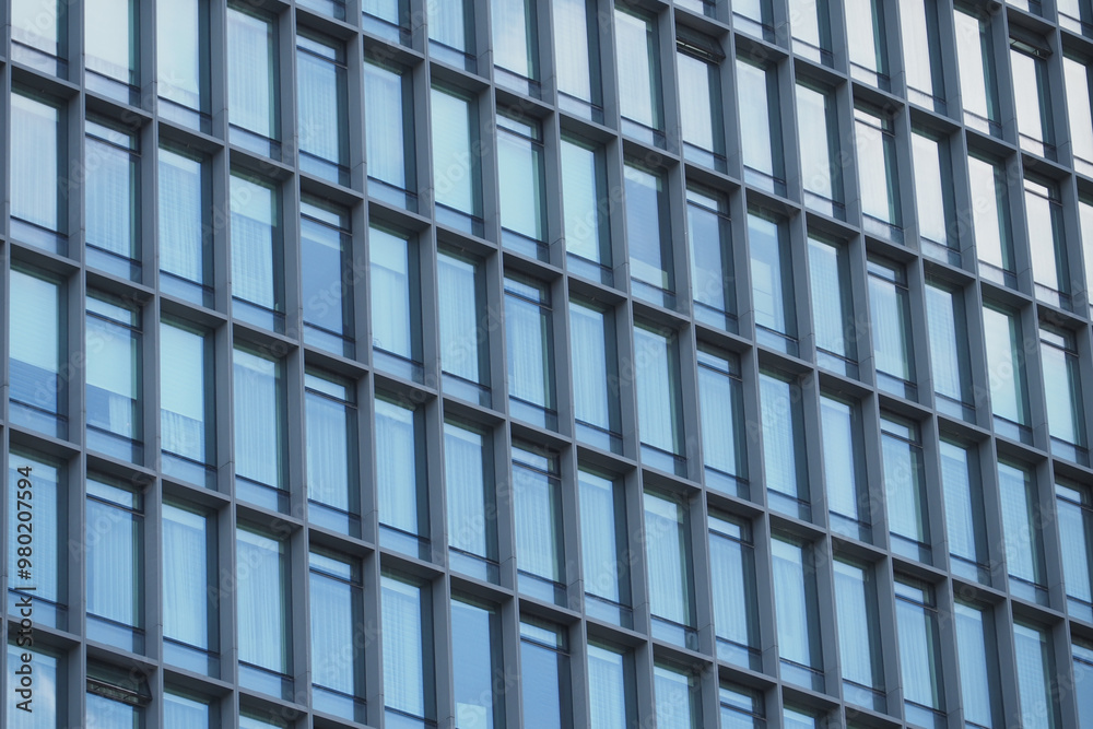 A modern office building facade with large glass windows that reflect its surroundings A modern office building facade with large glass windows that reflect its surroundings