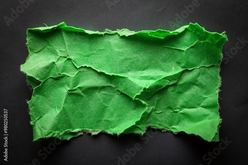 Torn and frayed green paper edge, ripped from a sheet, lies isolated against a dark black background, emphasizing the rough, unfinished, and discarded nature. photo