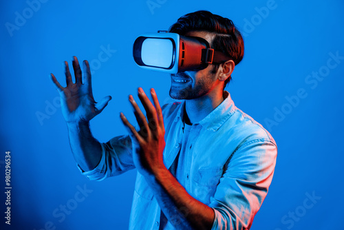 Caucasian smart man holding and moving gesture while using VR goggle. Happy person using headset and goggle while enter virtual world or metaverse with neon light background. Technology. Deviation.