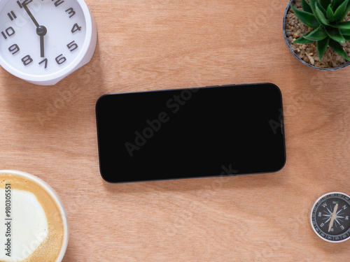 Blank mobile phone black screen isolated for mockup. coffee cup, cactus, clock on wooden workplace. Top view composition, concept online shopping, blog, logo, product, and social media.  . photo