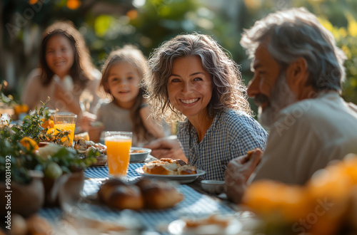 A joyful family enjoys a sunny garden lunch, with a grandmother smiling warmly as a man offers her orange juice.