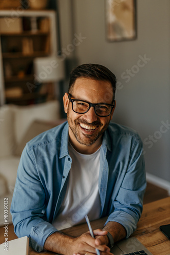 Portrait of a smiling handsome mid aged man, sitting at home and working on his laptop