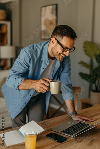 A man working from home over a laptop standing over the wooden table.