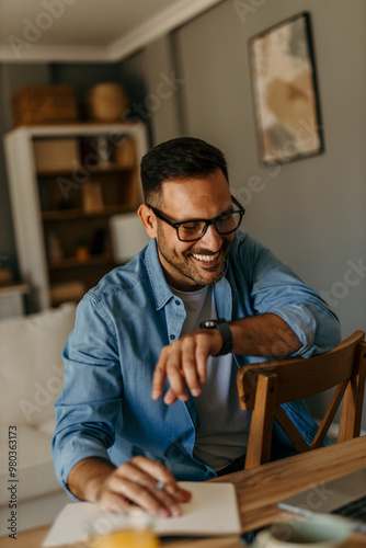 A smiling male freelancer with eyeglasses using a laptop while working from home