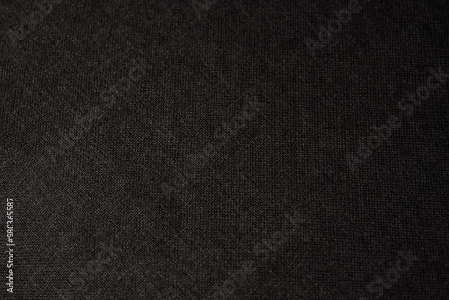 Dark textured fabric background with subtle weave patterns capturing warm light