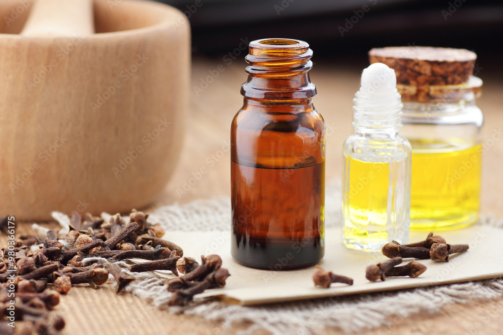 Cloves essential oil or extract in glass bottle with spice buds on wooden table, closeup, natural medicine and healthy skin and body treatment concept Cloves essential oil or extract in glass bottle with spice buds on wooden table, closeup, natural medicine and healthy skin and body treatment concept