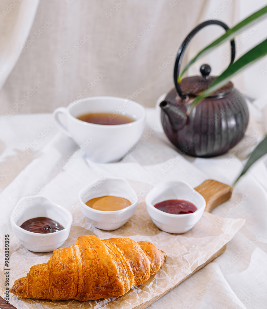 Freshly baked croissant served on wooden board with jam and tea for breakfast Freshly baked croissant served on wooden board with jam and tea for breakfast