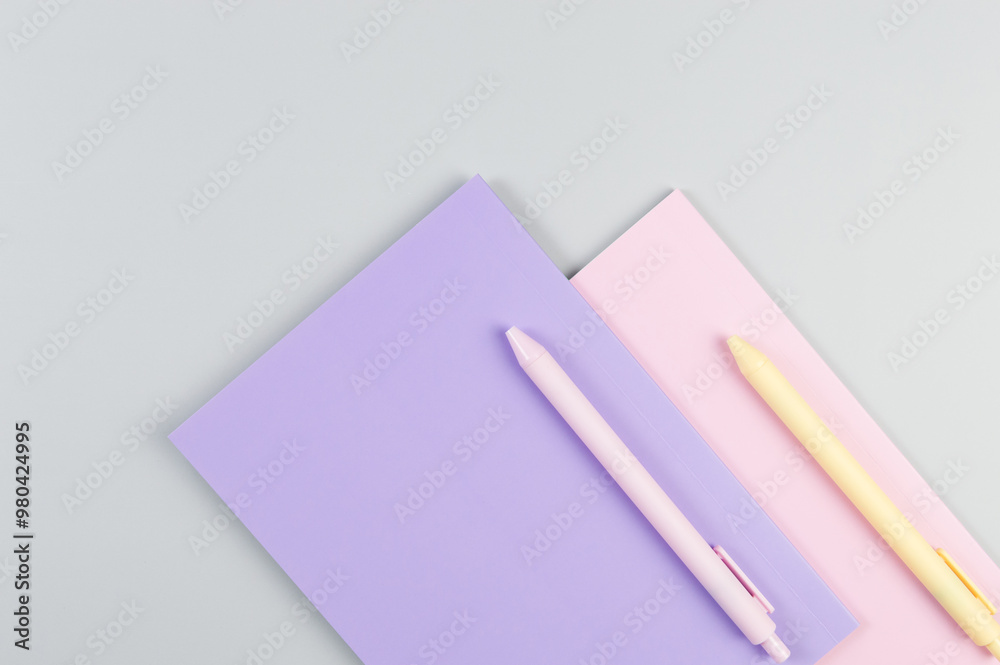 Top view of pink and purple notebooks on grey background. Pink and yellow pens, school, office wallpaper. Flat lay, copy space. Top view of pink and purple notebooks on grey background. Pink and yellow pens, school, office wallpaper. Flat lay, copy space.