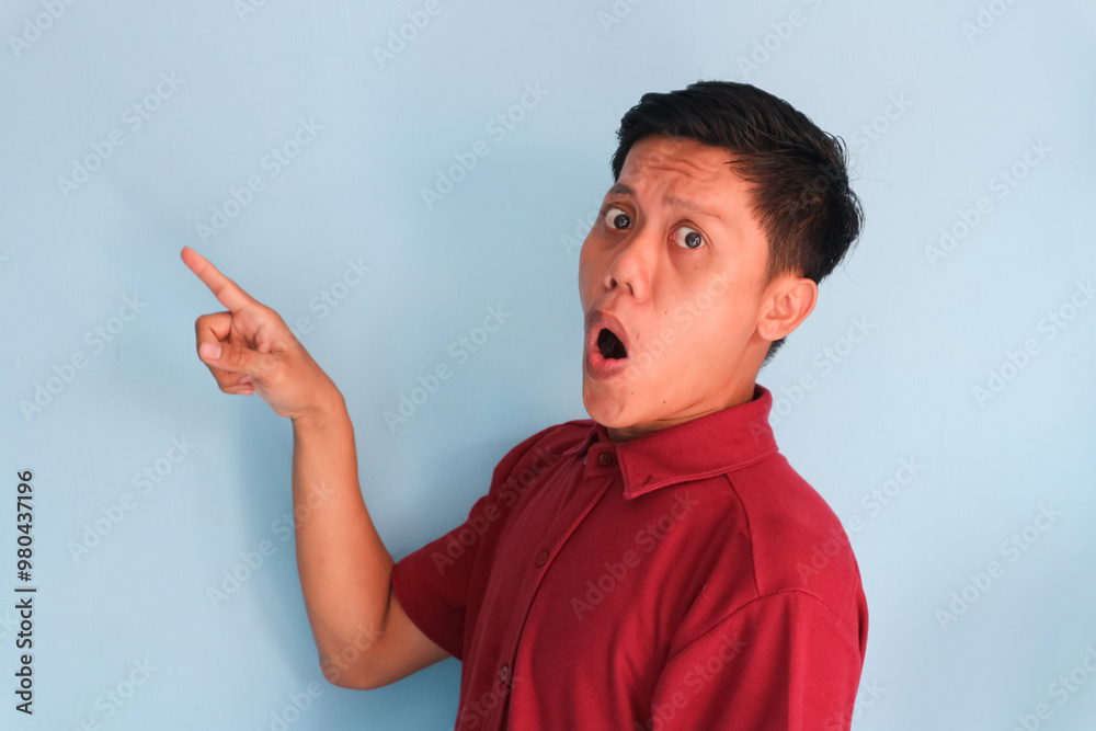 Surprised face of young Asian man in red shirt pointing finger to the side Surprised face of young Asian man in red shirt pointing finger to the side