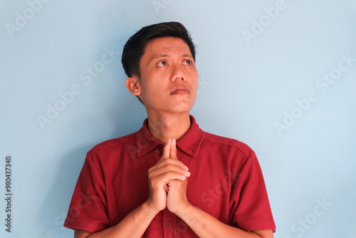 Asian young man wearing a red shirt showing thinking something gesture with his eyes looking up photo