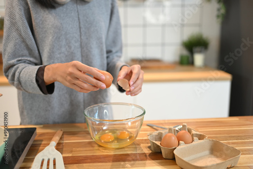 Young woman cracking an egg into a mixing bowl, preparing breakfast in her kitchen photo