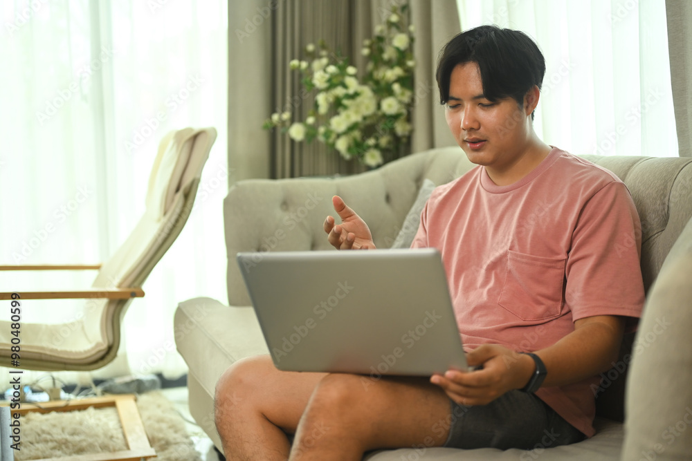 Asian man freelancer in casual clothes using laptop for video call, sitting on sofa at home Asian man freelancer in casual clothes using laptop for video call, sitting on sofa at home