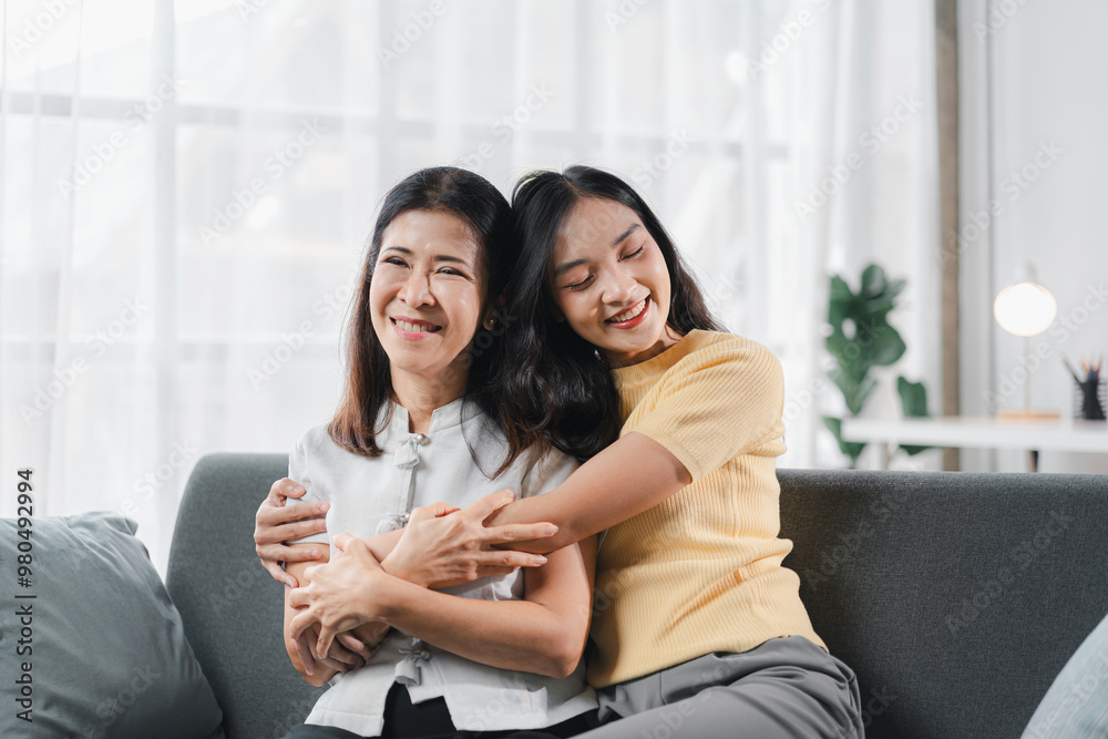 Cheerful spending time together of asian daughter hugging her mother laughing embracing happy senior aged mom having fun at living room home Cheerful spending time together of asian daughter hugging her mother laughing embracing happy senior aged mom having fun at living room home