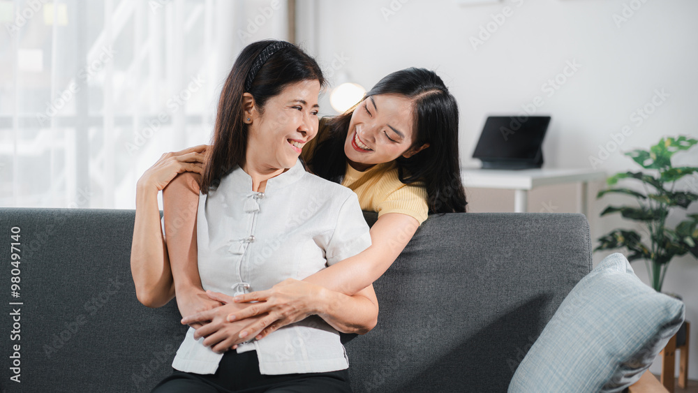 Obraz premium Cheerful spending time together of asian daughter hugging her mother laughing embracing happy senior aged mom having fun at living room home