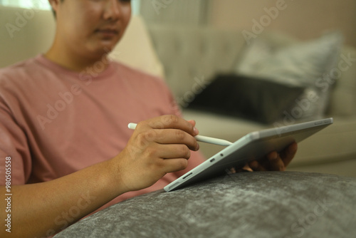 Cropped shot smiling young man using digital tablet sitting on sofa at home