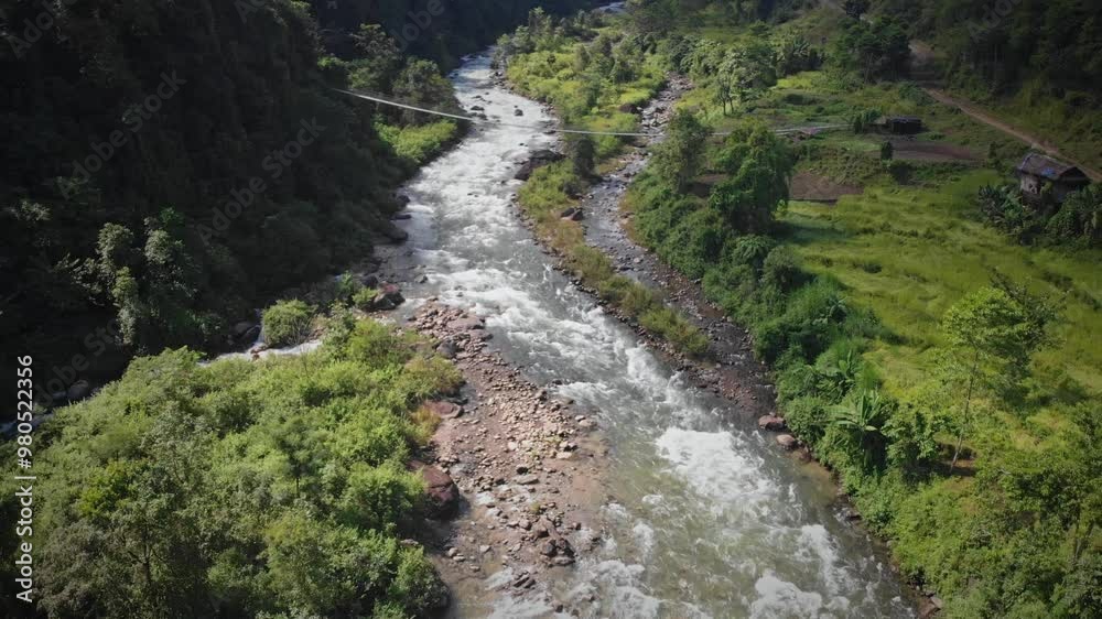 Drone shot of a suspension bridge over a small river, with paddy fields in a village in Bhojpur, Nepal Drone shot of a suspension bridge over a small river, with paddy fields in a village in Bhojpur, Nepal