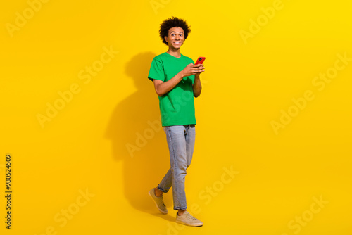 Full length photo of cheerful positive guy dressed green t-shirt communcating modern gadget emtpy space isolated yellow color background