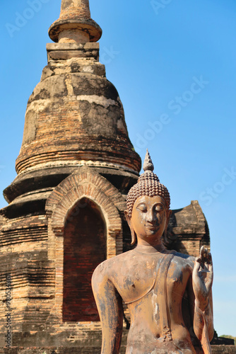 Photography Close up of the standing buddha statue in front of a small pagoda next to the Wa