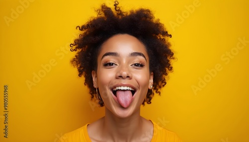 Happy young woman with afro hair sticking out her tongue against yellow background. photo