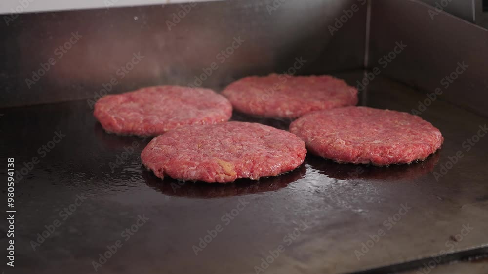 Close-up of four burger patties fried on a hot industrial stove in the restaurant kitchen. The process of cooking juicy mouth-watering burgers. Fast food. Close-up of four burger patties fried on a hot industrial stove in the restaurant kitchen. The process of cooking juicy mouth-watering burgers. Fast food.