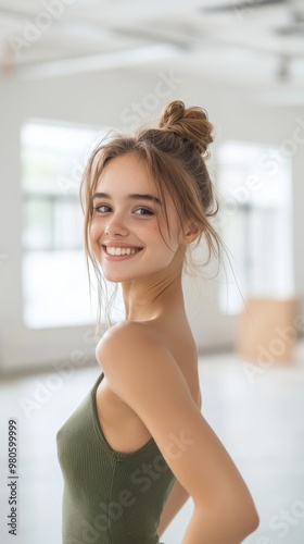 A young woman with a bright smile looks over her shoulder in a casual pose. She has a messy bun and is wearing a green tank top. The background is a blurred white space. Free Download A young woman with a bright smile looks over her shoulder in a casual pose. She has a messy bun and is wearing a green tank top. The background is a blurred white space. - GFXLoad