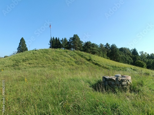 Bubiai hill during sunny day. Small hill. Grass is growing on hill. Staircase leading to the top. Sunny day with white and gray clouds in sky. Nature. Bubiu piliakalnis.	
 photo