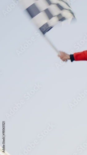 Racing marshal waving Checkered race at finish line on a raceway. Victory, achievement, success and sport concept. Grand Prix. Slow Motion. Vertical frame.