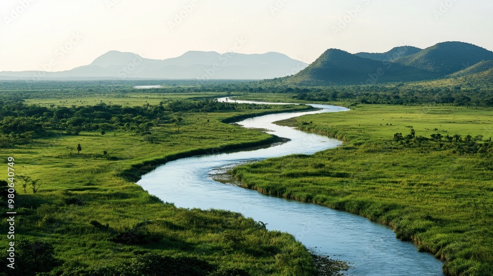 A wide, winding river cutting through a lush green valley, with distant mountains in the background under a clear sky. A wide, winding river cutting through a lush green valley, with distant mountains in the background under a clear sky.