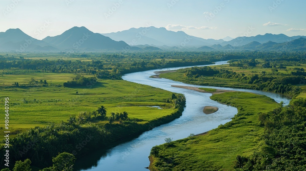 Obraz premium A wide, winding river cutting through a lush green valley, with distant mountains in the background under a clear sky.