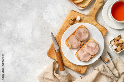 Obraz na płótnie Bread with turkey ham in a white plate closeup. Toasts with sausage for breakfast on a bright table w salonie
