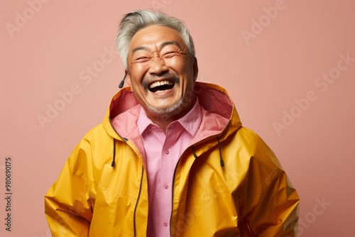 Portrait of a joyful asian man in his 60s wearing a functional windbreaker on pastel brown background