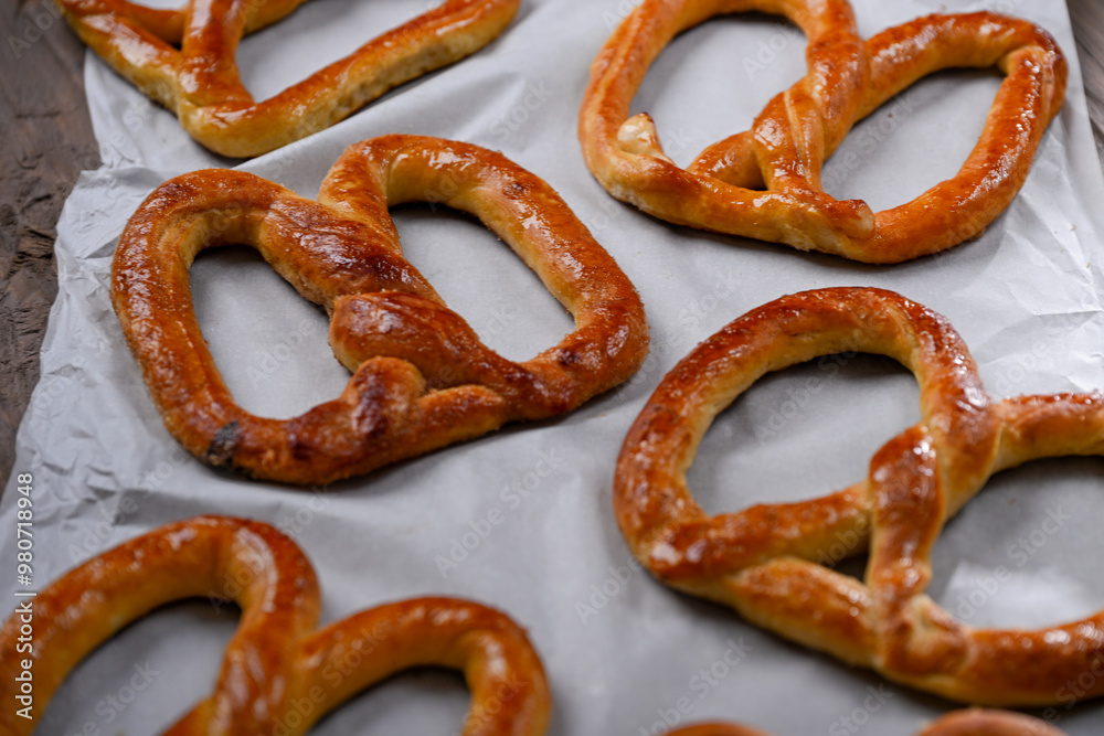 A close-up shot of freshly baked, golden-brown pretzels resting on parchment paper. The pretzels have a glossy, and the wooden background adds a rustic charm to this appetizing scene A close-up shot of freshly baked, golden-brown pretzels resting on parchment paper. The pretzels have a glossy, and the wooden background adds a rustic charm to this appetizing scene