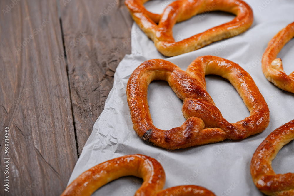 A close-up shot of freshly baked, golden-brown pretzels resting on parchment paper. The pretzels have a glossy, and the wooden background adds a rustic charm to this appetizing scene A close-up shot of freshly baked, golden-brown pretzels resting on parchment paper. The pretzels have a glossy, and the wooden background adds a rustic charm to this appetizing scene