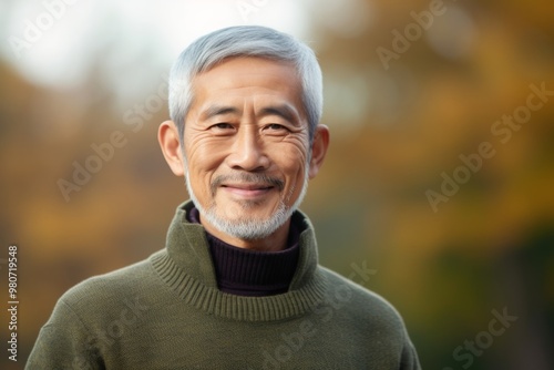 Portrait of a tender asian man in his 80s wearing a cozy sweater in soft green background