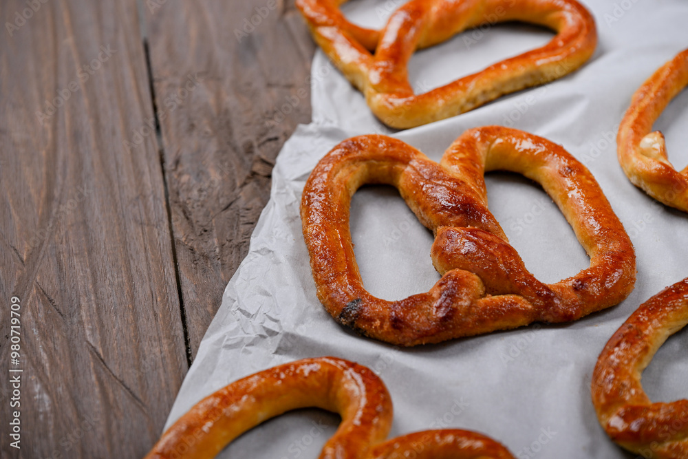 A close-up shot of freshly baked, golden-brown pretzels resting on parchment paper. The pretzels have a glossy, and the wooden background adds a rustic charm to this appetizing scene A close-up shot of freshly baked, golden-brown pretzels resting on parchment paper. The pretzels have a glossy, and the wooden background adds a rustic charm to this appetizing scene