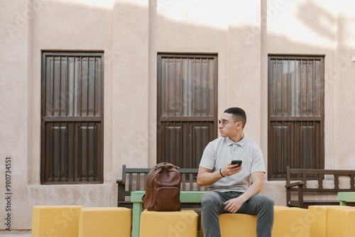 Young arab man sitting outdoors holding his phone in a hand. Generation Z concept