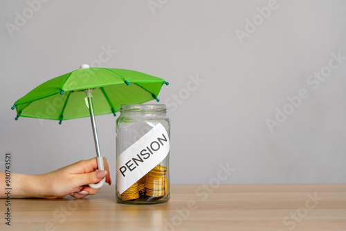 Bank of coins with the inscription Pension and green umbrella. Retirement Insurance concept. Financial support and regular payments to people after retirement. Business and finance